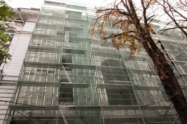 Historic-centre commercial building: protective mesh and scaffolding along the façade. Site-report photograph.